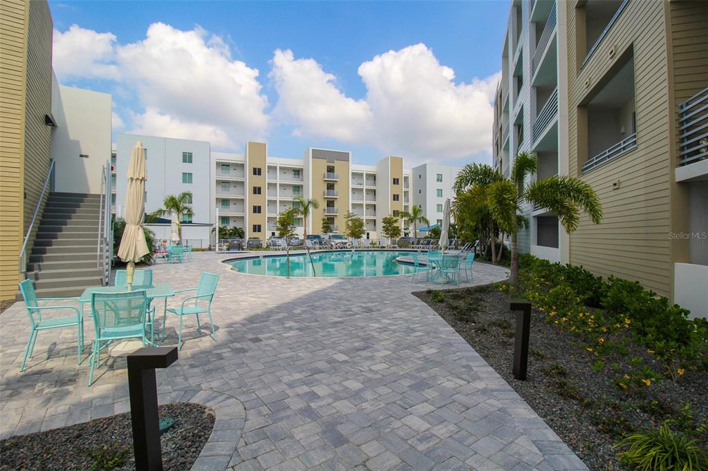 An outdoor swimming pool area with patio furniture and multi-story apartment buildings in the background — 1703 N TAMIAMI TRAIL UNIT B406, SARASOTA, FL
