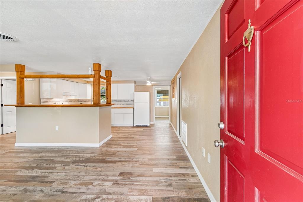 An interior view shows a red front door opening into a living area with wood-look flooring — 5046 FARLEY DRIVE, HOLIDAY, FL