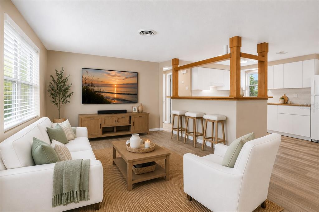 A living room with a white sofa and armchair faces a television and kitchen bar — 5046 FARLEY DRIVE, HOLIDAY, FL