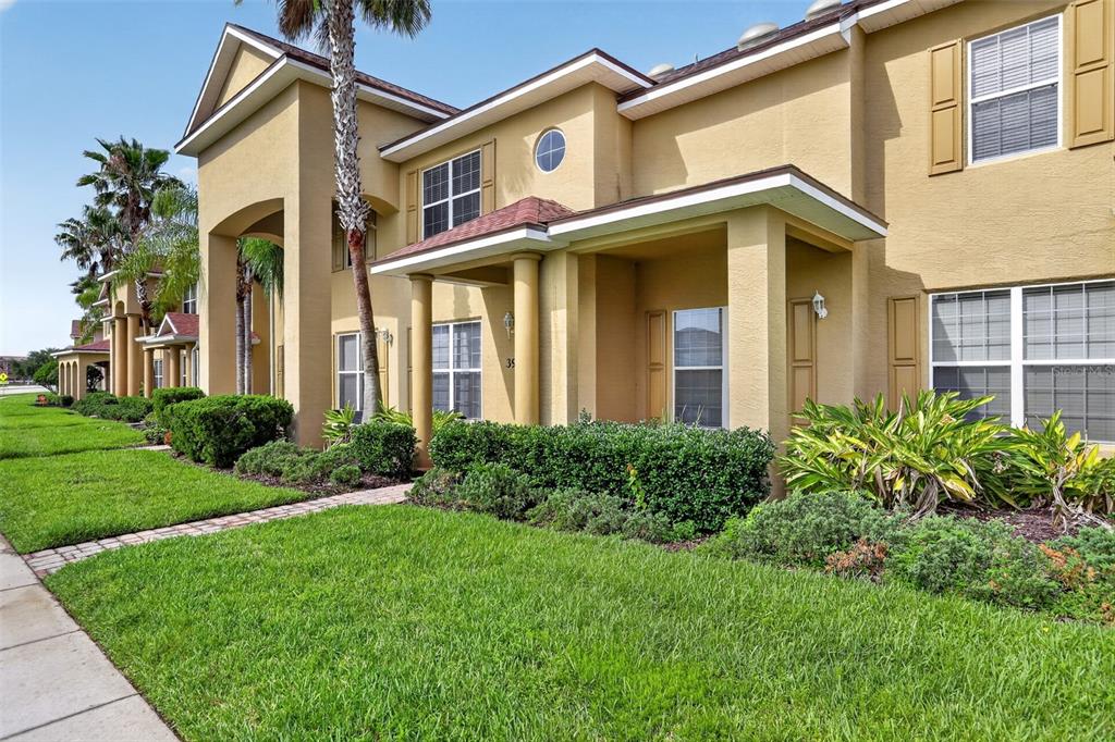 A two-story tan stucco townhouse with a covered entryway and manicured landscaping — 390 N AIRPORT ROAD, NEW SMYRNA BEACH, FL