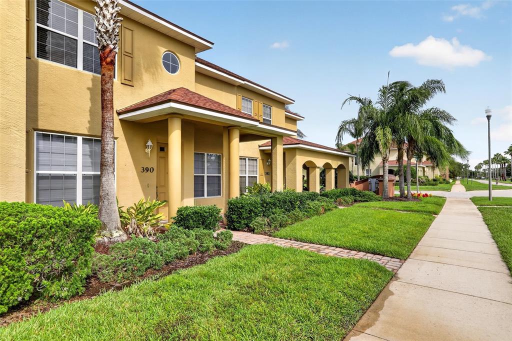 A two-story yellow stucco townhouse with a covered entryway and a sidewalk in front — 390 N AIRPORT ROAD, NEW SMYRNA BEACH, FL