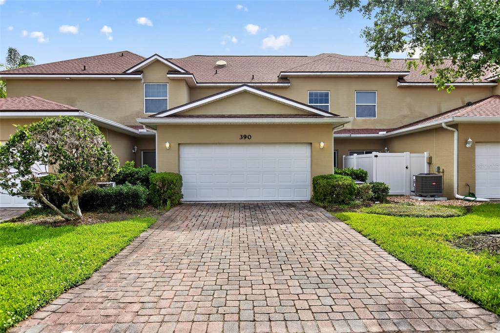 A two-story townhouse with a tan stucco exterior, a white garage door, and a paver driveway — 390 N AIRPORT ROAD, NEW SMYRNA BEACH, FL