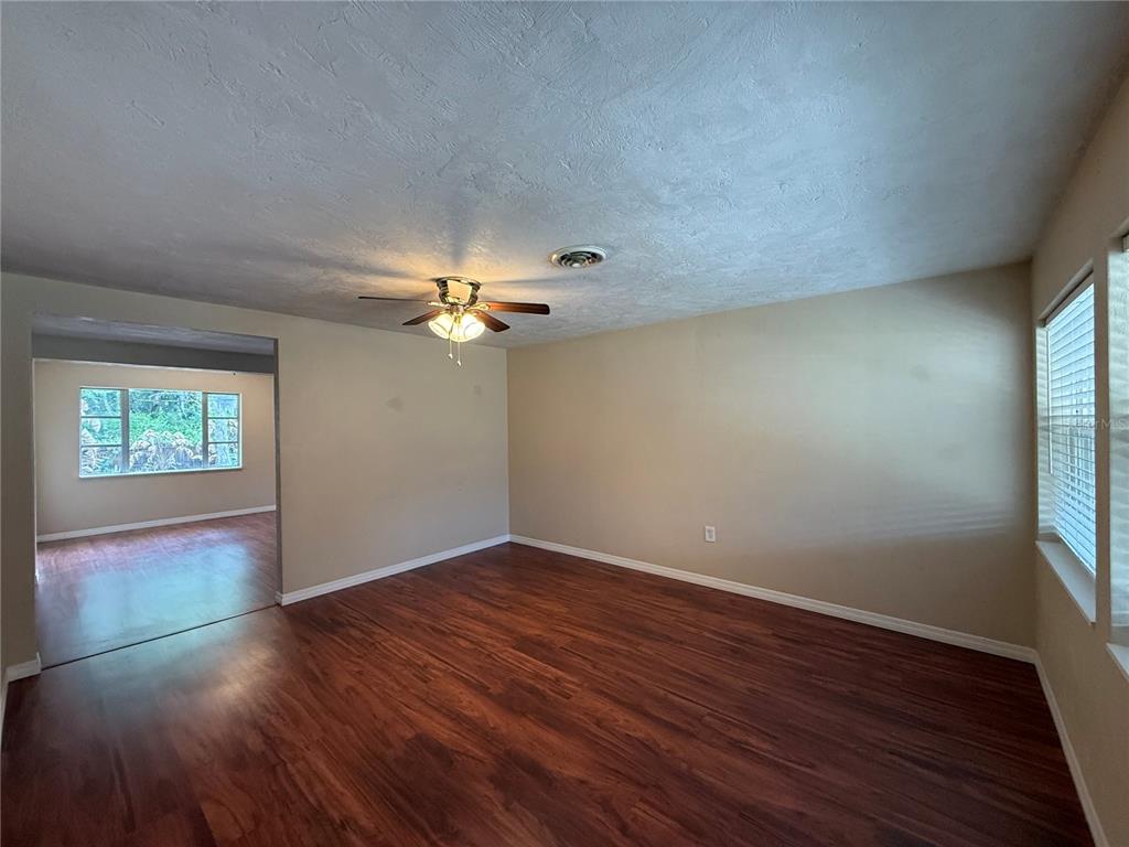 An empty living room features wood-look flooring, beige walls, a ceiling fan, and large windows — 438 PERDITA AVENUE, EDGEWATER, FL