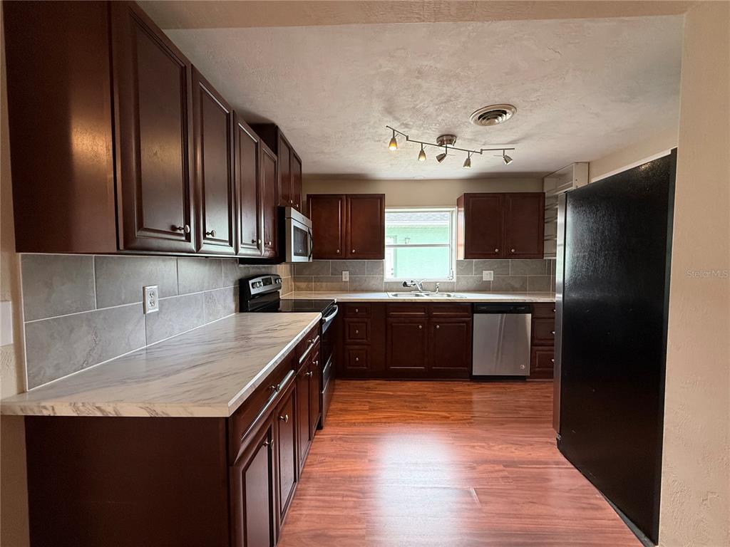 A kitchen features dark wood cabinets, white marble-patterned countertops, stainless steel appliances, and wood flooring — 438 PERDITA AVENUE, EDGEWATER, FL
