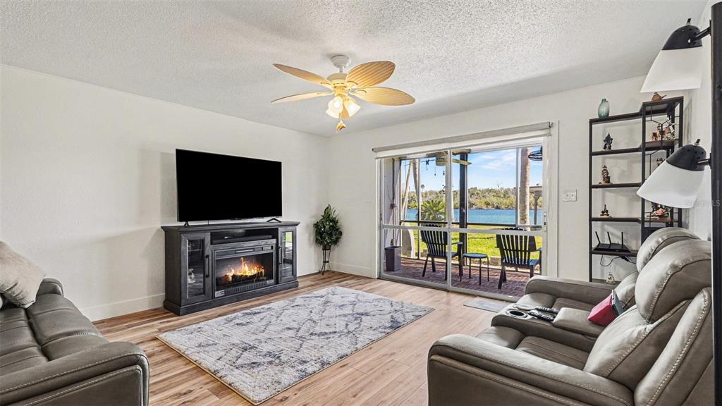 A living room features a fireplace, a ceiling fan, and sliding doors overlooking a lake — 10684 W HALLS RIVER ROAD UNIT 2, HOMOSASSA, FL