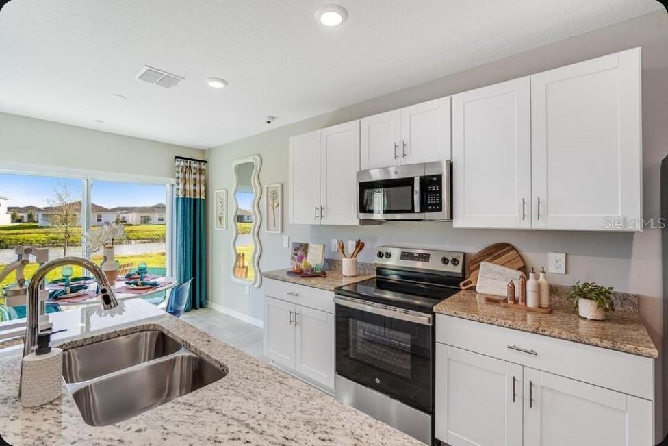 A kitchen with white cabinets, granite countertops, stainless steel appliances, and a view of water — 6518 EQUINOX LANE, NORTH FORT MYERS, FL
