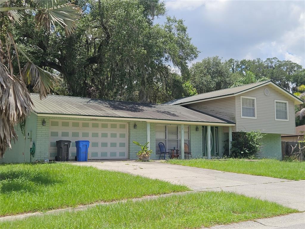 A two-story house with a light green brick exterior, metal roof, and attached two-car garage — 1203 LAKE VALRICO LANE, VALRICO, FL