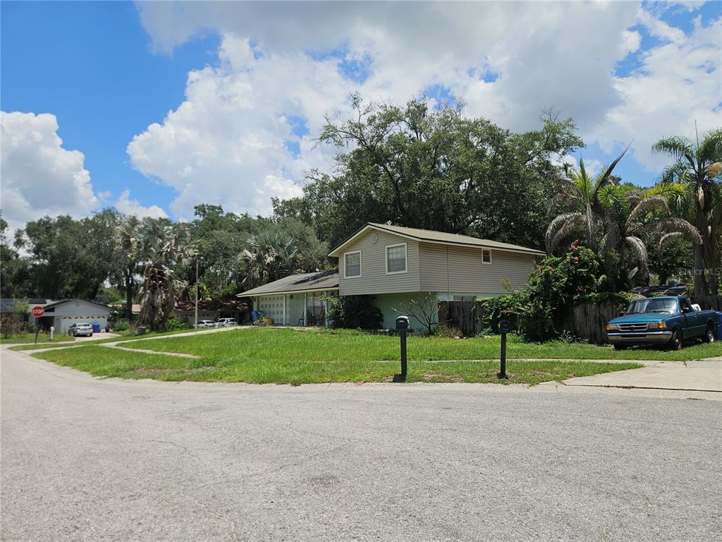 A two-story house with light-colored siding and a garage sits on a grassy corner lot — 1203 LAKE VALRICO LANE, VALRICO, FL