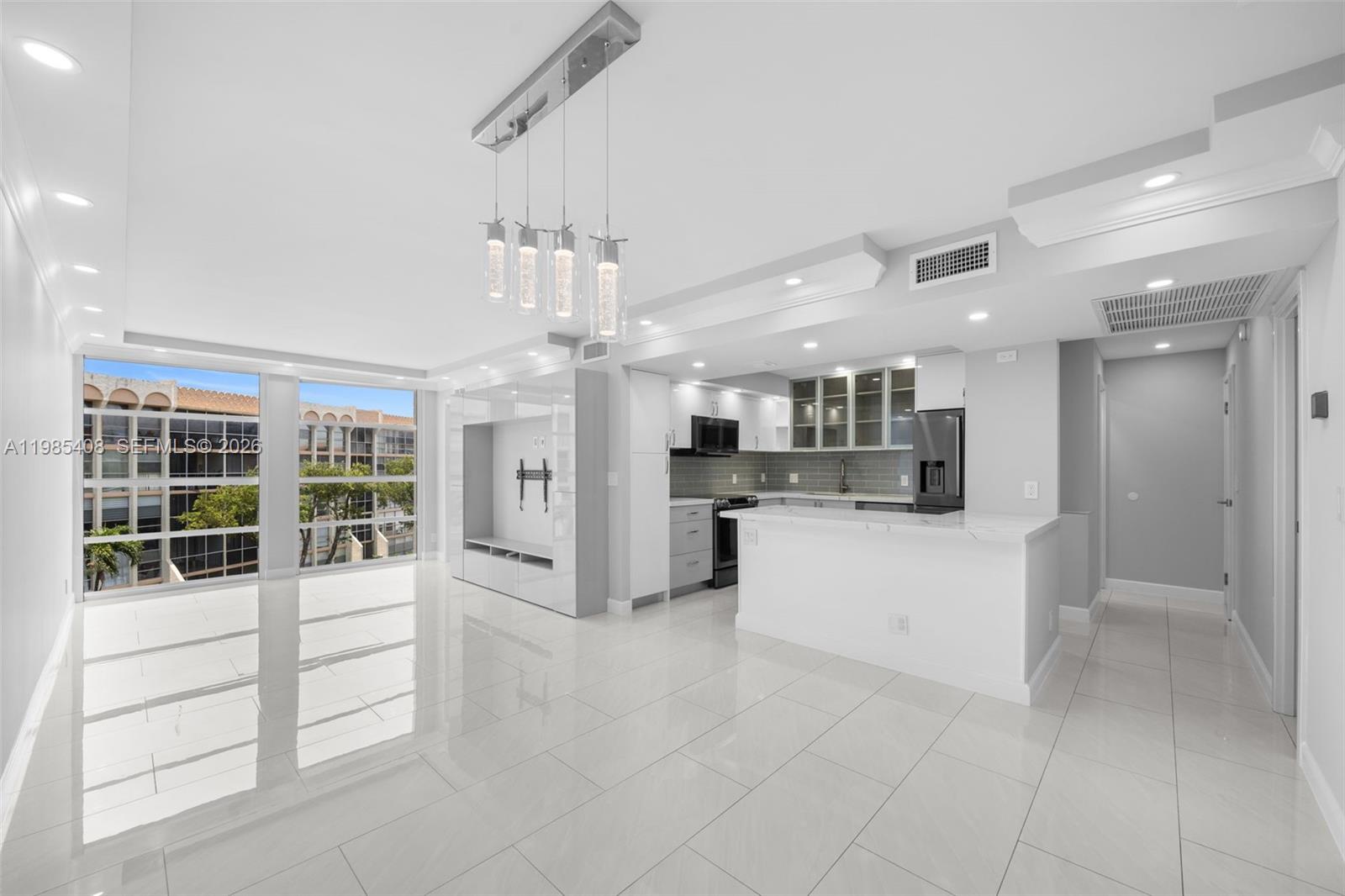 A modern, open-concept kitchen and living area features white tile floors and a breakfast bar — 701 Three Islands Blvd # 411, Hallandale Beach FL 33009, HALLANDALE BEACH, FL