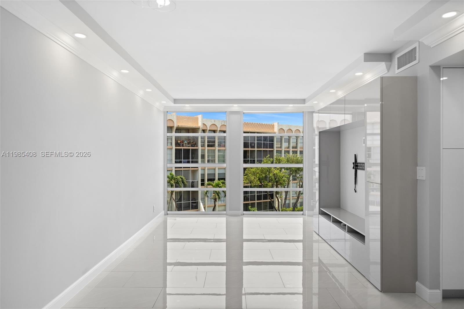 A bright, empty room features white tile floors, recessed lighting, and a built-in media console — 701 Three Islands Blvd # 411, Hallandale Beach FL 33009, HALLANDALE BEACH, FL