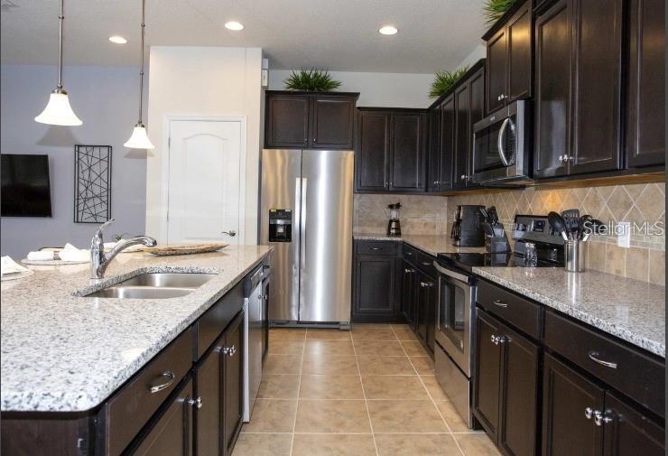 A kitchen features dark wood cabinets, granite countertops, stainless steel appliances, and a center island — 8875 GENEVE CT, KISSIMMEE, FL