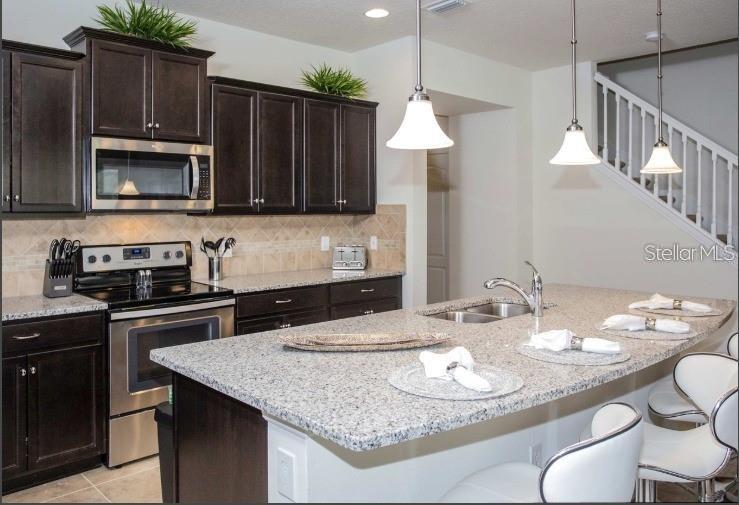 A kitchen features dark wood cabinets, granite countertops, a center island, and stainless steel appliances — 8875 GENEVE CT, KISSIMMEE, FL