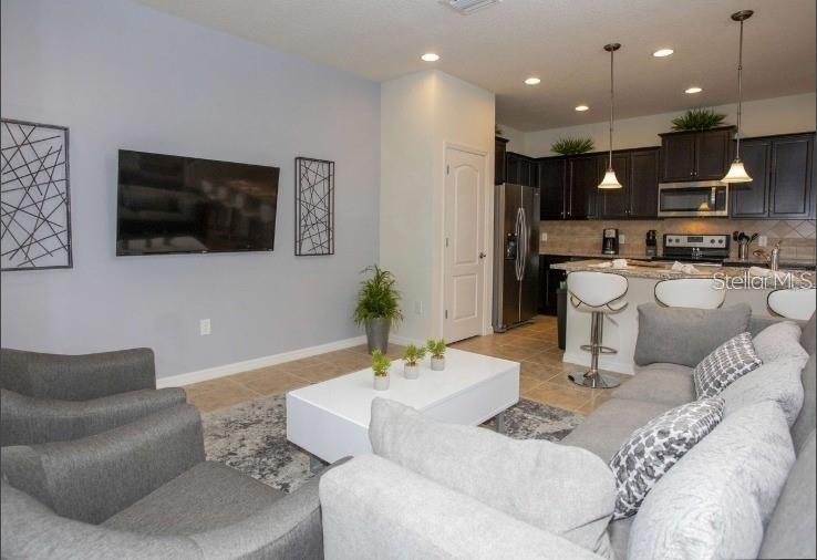 An open-concept living room features gray furniture, a white coffee table, and an adjacent kitchen — 8875 GENEVE CT, KISSIMMEE, FL