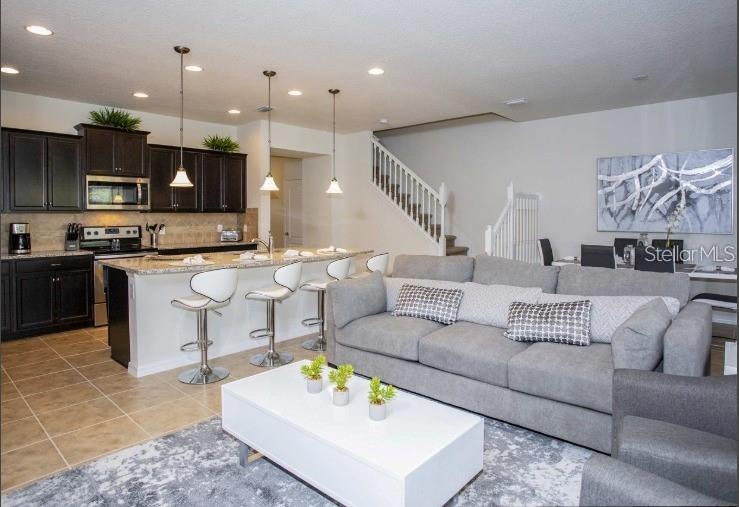 An open-concept kitchen with dark cabinets and a breakfast bar overlooks a living room area — 8875 GENEVE CT, KISSIMMEE, FL