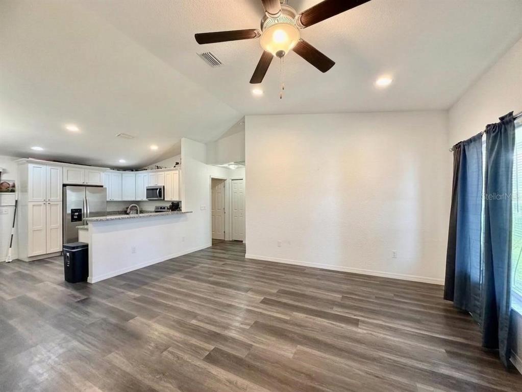 An open-concept living area features wood-look flooring, a ceiling fan, and an adjacent white kitchen — 48 MAPLE DRIVE, OCKLAWAHA, FL