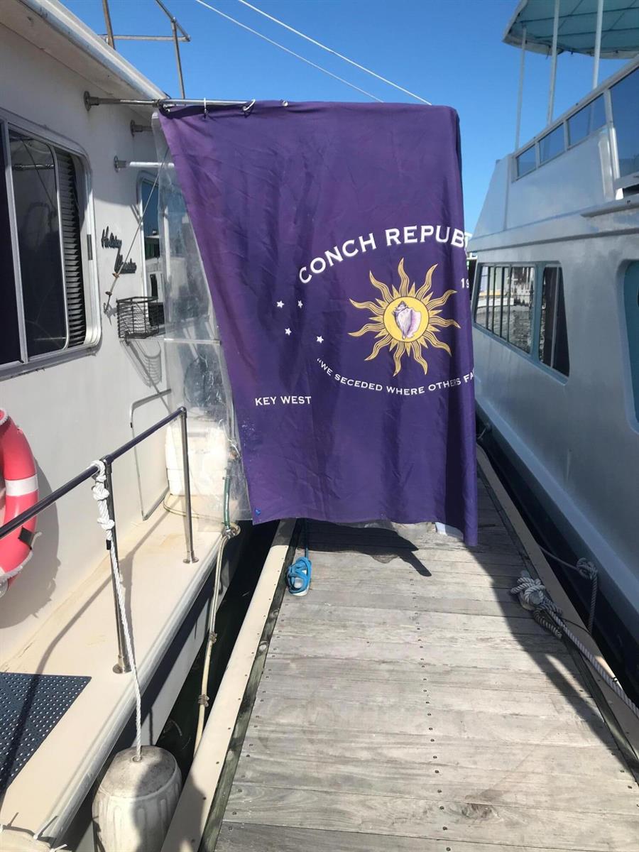 A purple Conch Republic flag hangs from a boat docked at a wooden pier — 1801 N Roosevelt Boulevard, Key West FL 33040, KEY WEST, FL