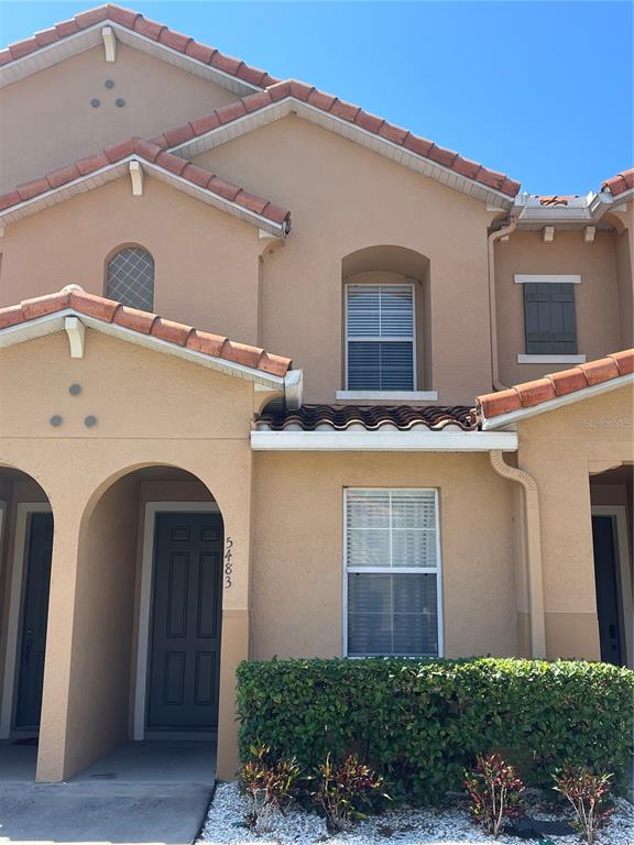 The exterior of a two-story tan stucco townhouse features a tiled roof and arched entryway — 5483 PARADISE CAY CIRCLE, KISSIMMEE, FL
