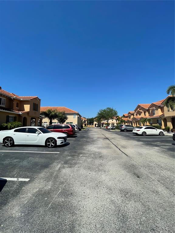 A parking lot sits between two rows of multi-story residential buildings under a clear sky — 5483 PARADISE CAY CIRCLE, KISSIMMEE, FL