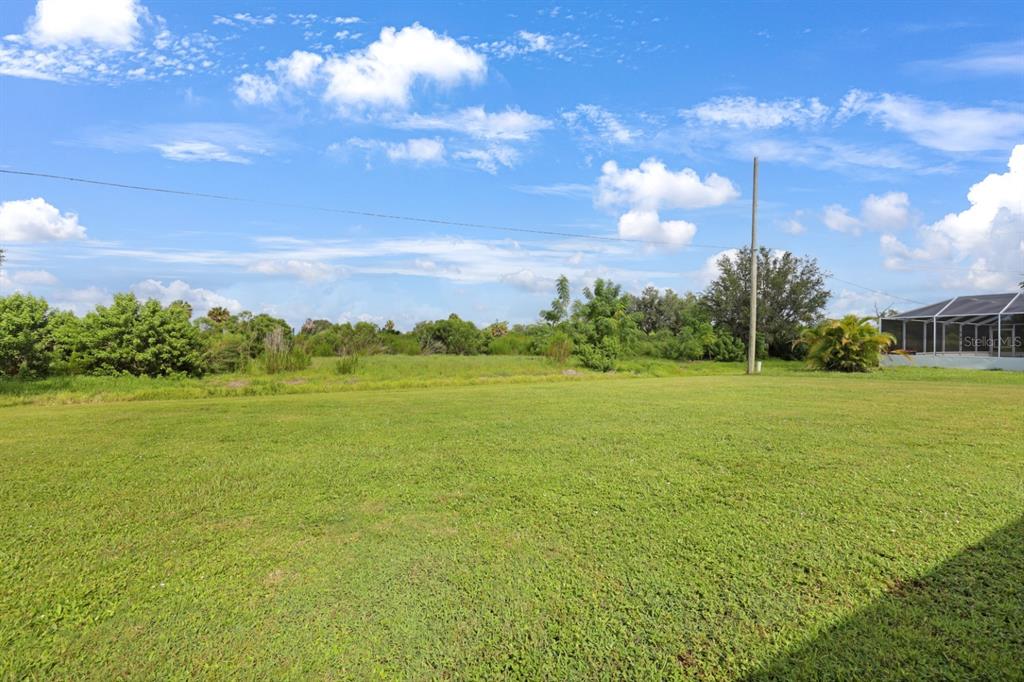 A large, grassy backyard features a utility pole and a screened-in patio on the right — 2219 BEACON DRIVE, PORT CHARLOTTE, FL