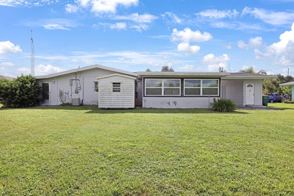 The exterior view of a single-story house features a large lawn, a shed, and windows — 2219 BEACON DRIVE, PORT CHARLOTTE, FL