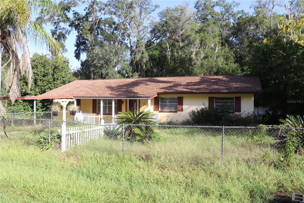 A single-story house with yellow siding and a brown roof sits behind a chain-link fence — 1855 NE 23 STREET, OCALA, FL