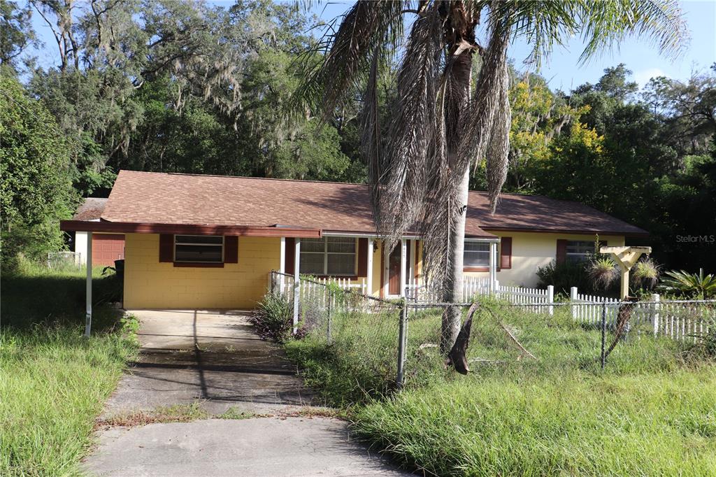 A single-story yellow house with a brown roof, carport, and a fenced front yard — 1855 NE 23 STREET, OCALA, FL