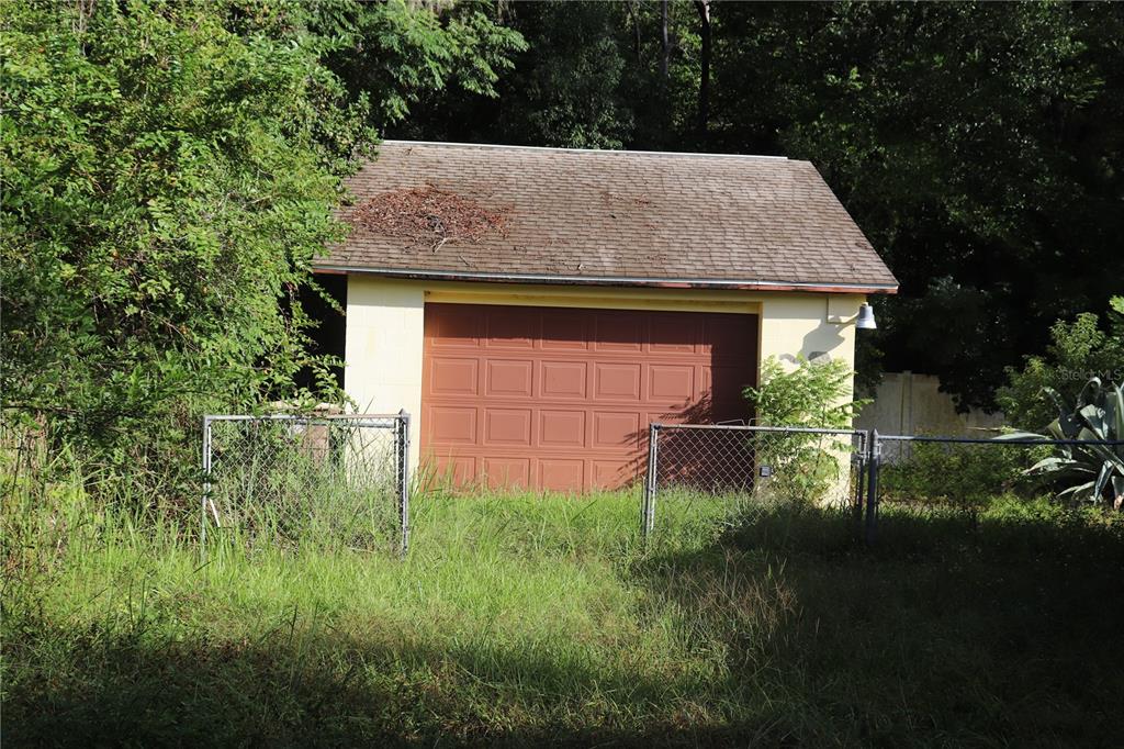 A detached garage with a brown door and shingled roof sits behind a chain-link fence — 1855 NE 23 STREET, OCALA, FL