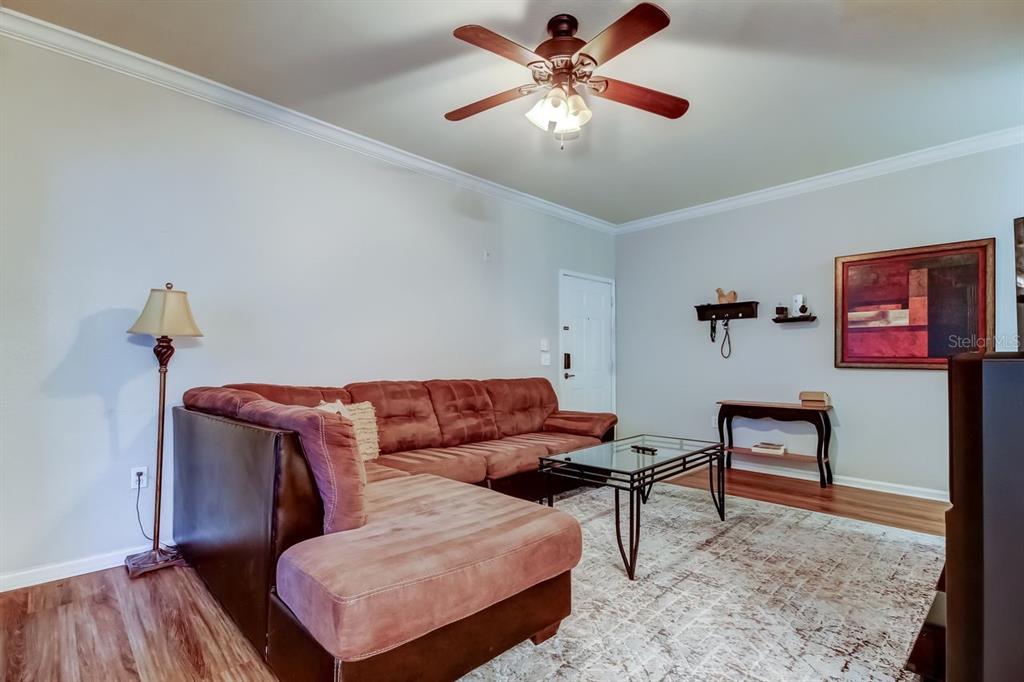 A living room features a brown sectional sofa, a glass coffee table, and a ceiling fan — 2279 PORTOFINO PLACE UNIT -2015, PALM HARBOR, FL