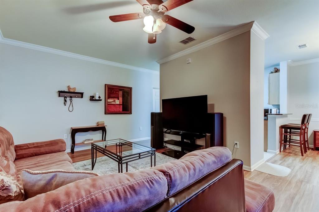 A living room features a brown sofa, glass coffee table, television, and ceiling fan — 2279 PORTOFINO PLACE UNIT -2015, PALM HARBOR, FL