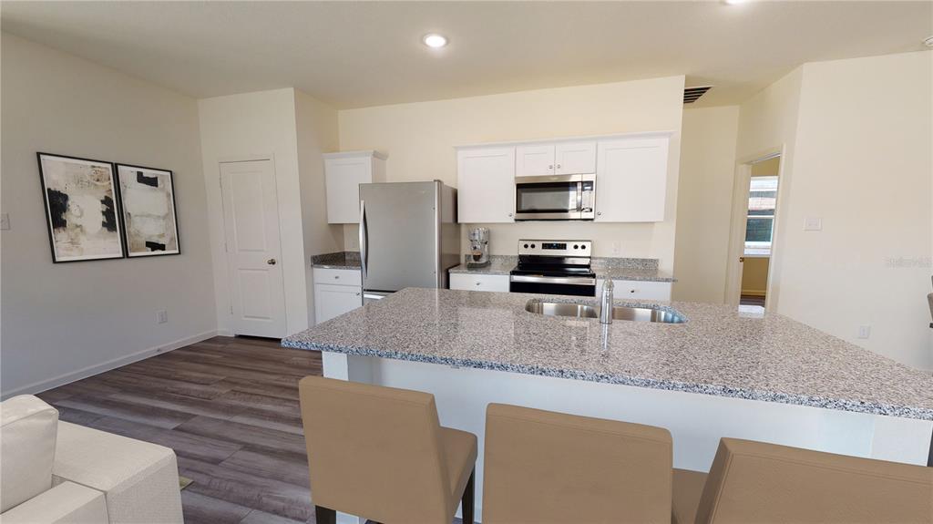 A kitchen features white cabinets, granite countertops, stainless steel appliances, and a central island — 10522 CURVING CREEK LOOP, PARRISH, FL