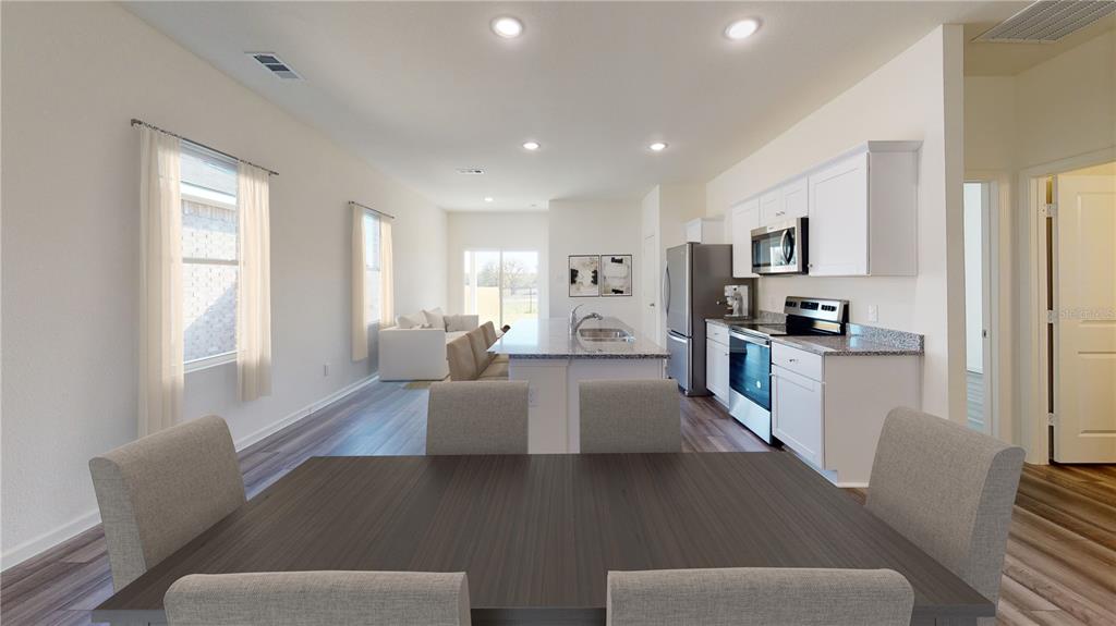A dining area opens to a kitchen with white cabinets, granite countertops, and stainless appliances — 10522 CURVING CREEK LOOP, PARRISH, FL