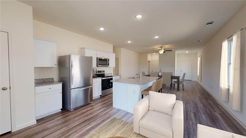 An open-concept kitchen features white cabinetry, stainless steel appliances, a granite island, and wood flooring — 10522 CURVING CREEK LOOP, PARRISH, FL