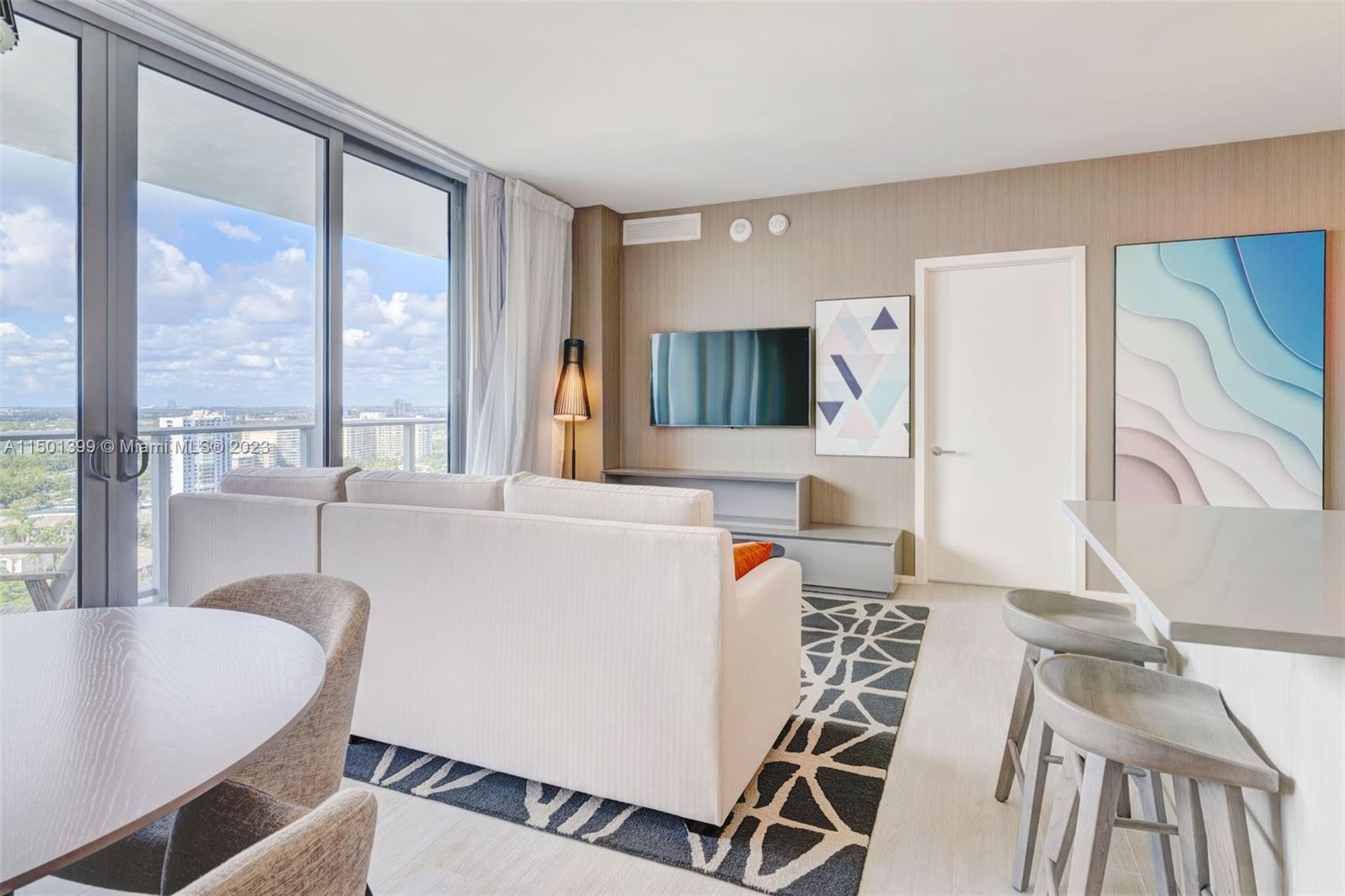 A modern living room features a white sofa, a television, and floor-to-ceiling windows with views — 4010 S Ocean Dr # R2106, Hollywood FL 33019, HOLLYWOOD, FL