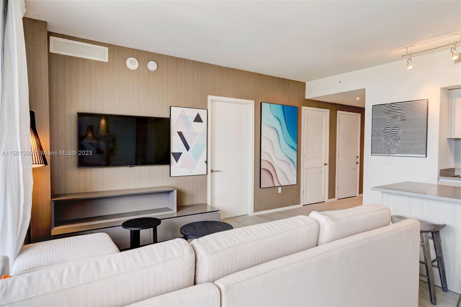 A living room features a wall-mounted television, a light-colored sofa, and modern wall art — 4010 S Ocean Dr # R2106, Hollywood FL 33019, HOLLYWOOD, FL