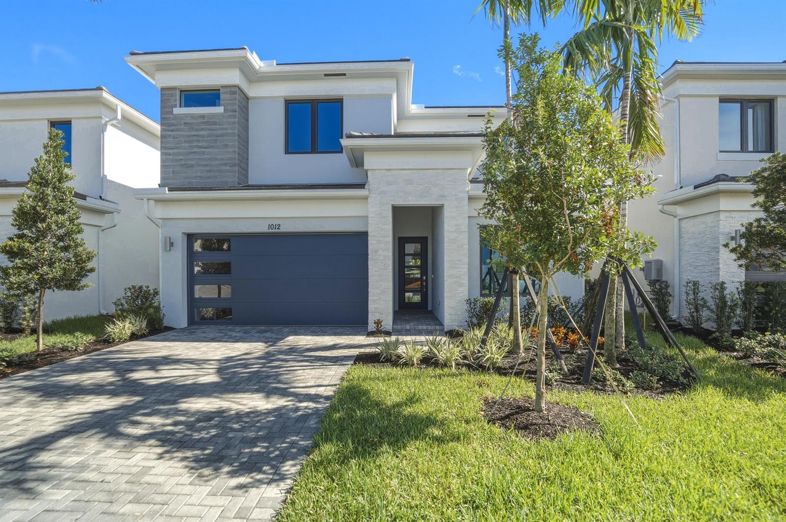 A two-story modern house features a gray garage door, white stone accents, and a paved driveway — 1012 Raleigh Way, Wellington FL 33414, WELLINGTON, FL
