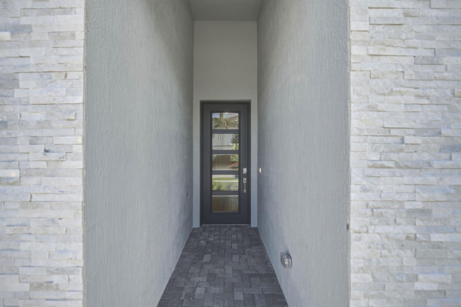 A narrow entryway features stone-clad walls, a paved floor, and a dark glass-paneled front door — 1012 Raleigh Way, Wellington FL 33414, WELLINGTON, FL