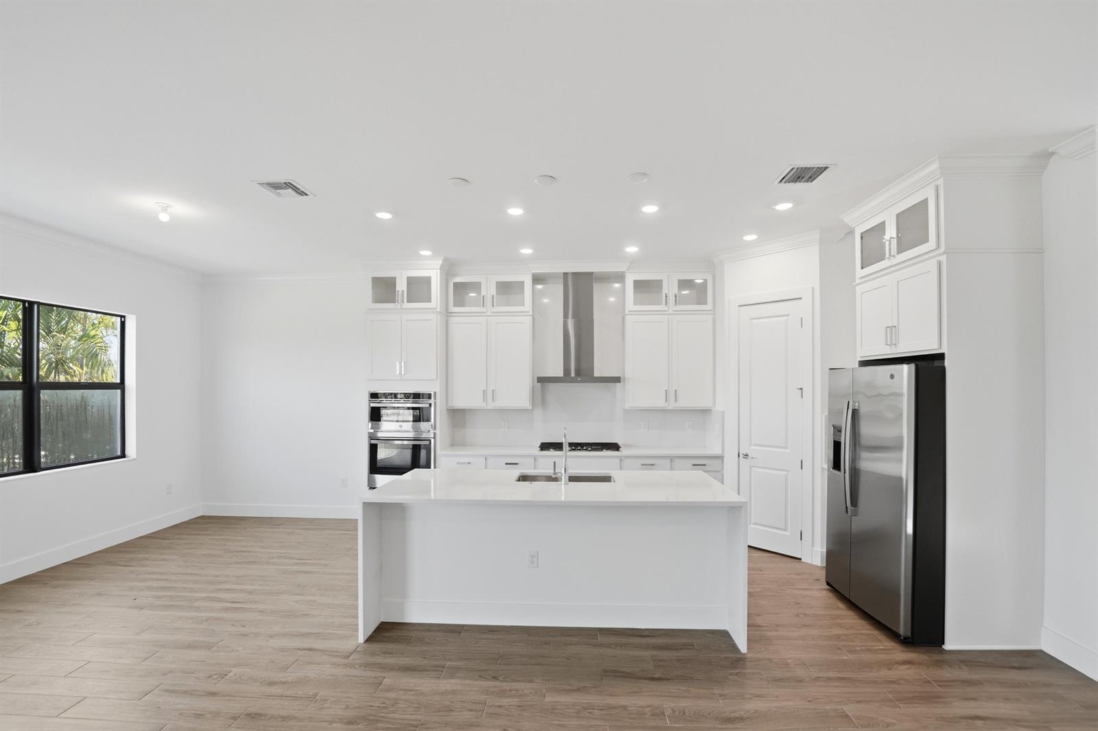 A modern kitchen features white cabinetry, stainless steel appliances, a center island, and wood-look flooring — 1012 Raleigh Way, Wellington FL 33414, WELLINGTON, FL