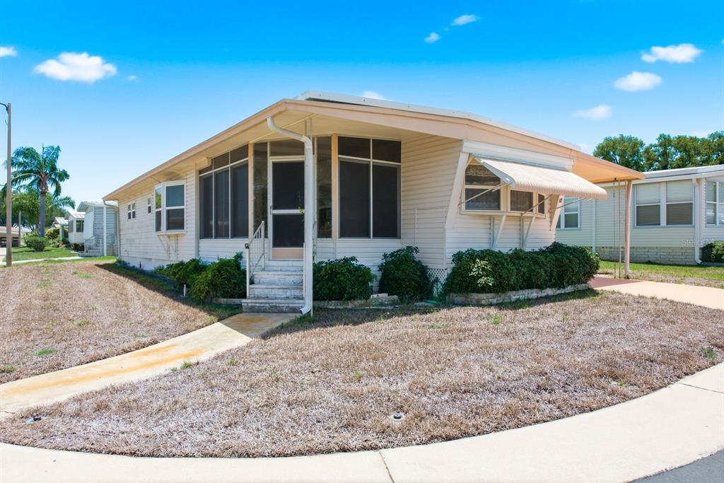 A single-story manufactured home with a carport, screened porch, and a front lawn — 39820 US HIGHWAY 19 N UNIT 67, TARPON SPRINGS, FL