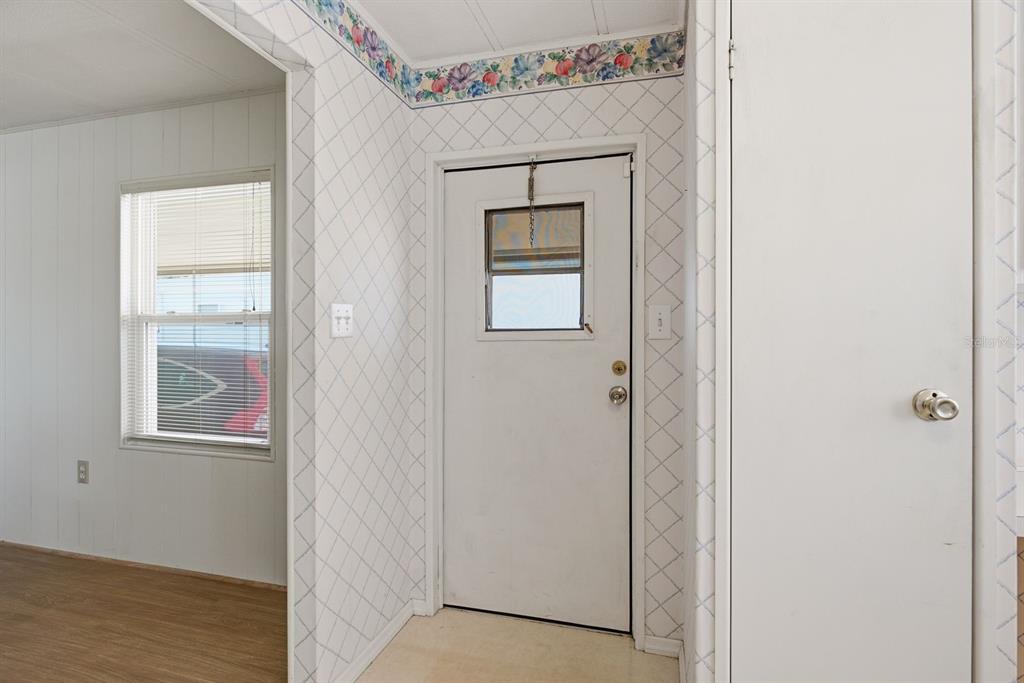 An entryway features white diamond-patterned wallpaper, a floral border, and a white exterior door — 39820 US HIGHWAY 19 N UNIT 67, TARPON SPRINGS, FL