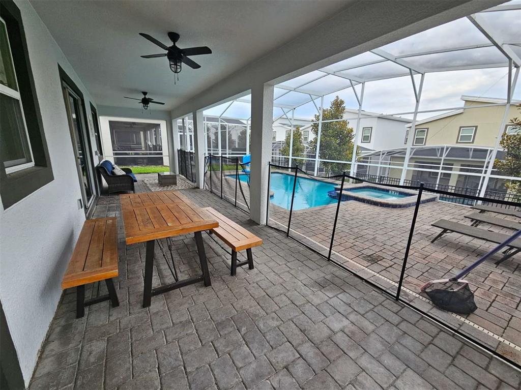 A covered patio features a wooden dining set, ceiling fans, and a screened-in pool area — 1241 CHALLENGE DRIVE, DAVENPORT, FL