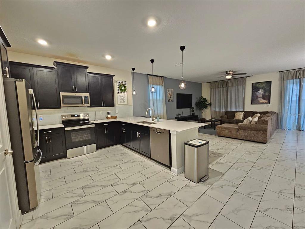 An open-concept kitchen with dark cabinets and white countertops flows into a living room area — 1241 CHALLENGE DRIVE, DAVENPORT, FL