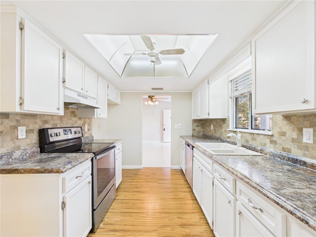 A galley kitchen features white cabinets, granite countertops, a tiled backsplash, and a ceiling fan — 8430 SW 105TH PLACE, OCALA, FL