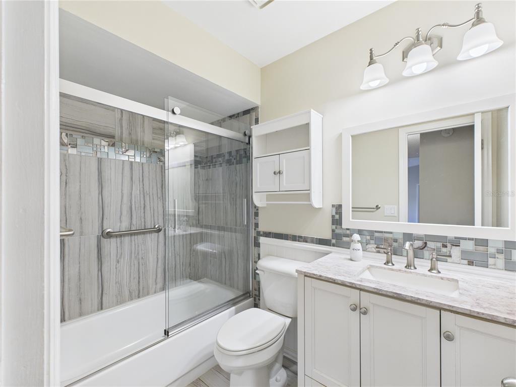 A bathroom features a glass-enclosed tub, a white vanity, a toilet, and gray tile accents — 8430 SW 105TH PLACE, OCALA, FL