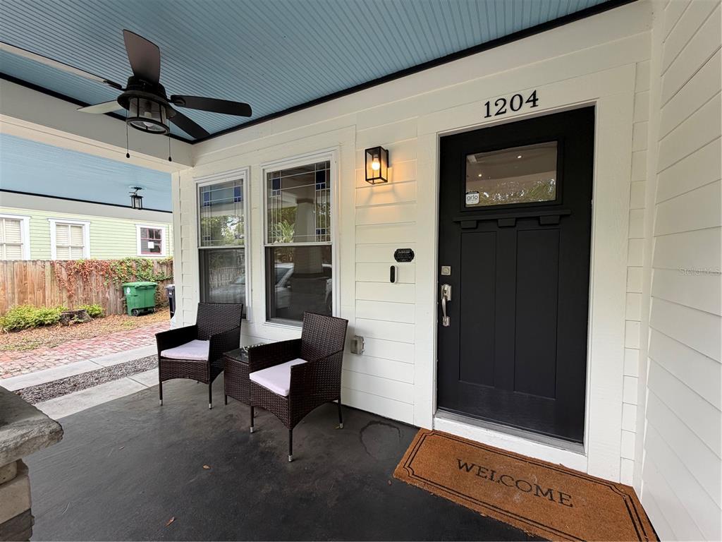 A covered front porch features a black door, two wicker chairs, and a ceiling fan — 1204 E ELLICOTT STREET, TAMPA, FL