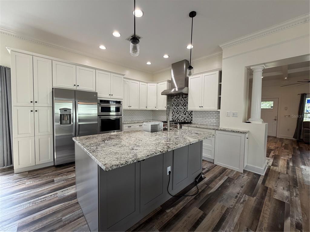 A kitchen features white cabinets, a gray island with granite countertops, and wood-look flooring — 1204 E ELLICOTT STREET, TAMPA, FL