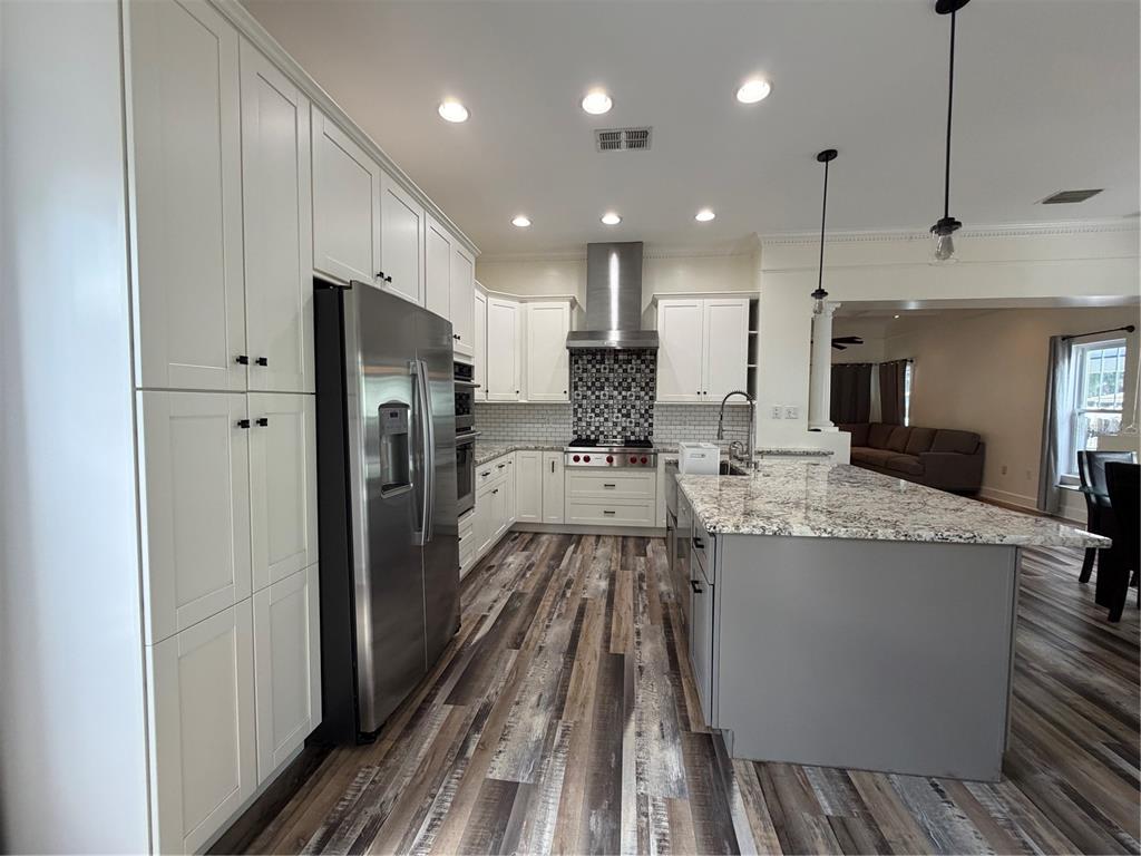 A kitchen features white cabinetry, stainless steel appliances, a granite-topped island, and wood-look flooring — 1204 E ELLICOTT STREET, TAMPA, FL