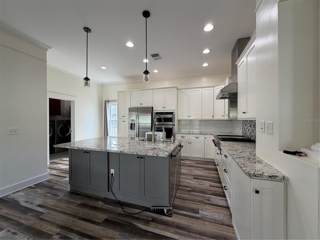 A kitchen features a gray island, white cabinets, granite countertops, and wood-look flooring — 1204 E ELLICOTT STREET, TAMPA, FL