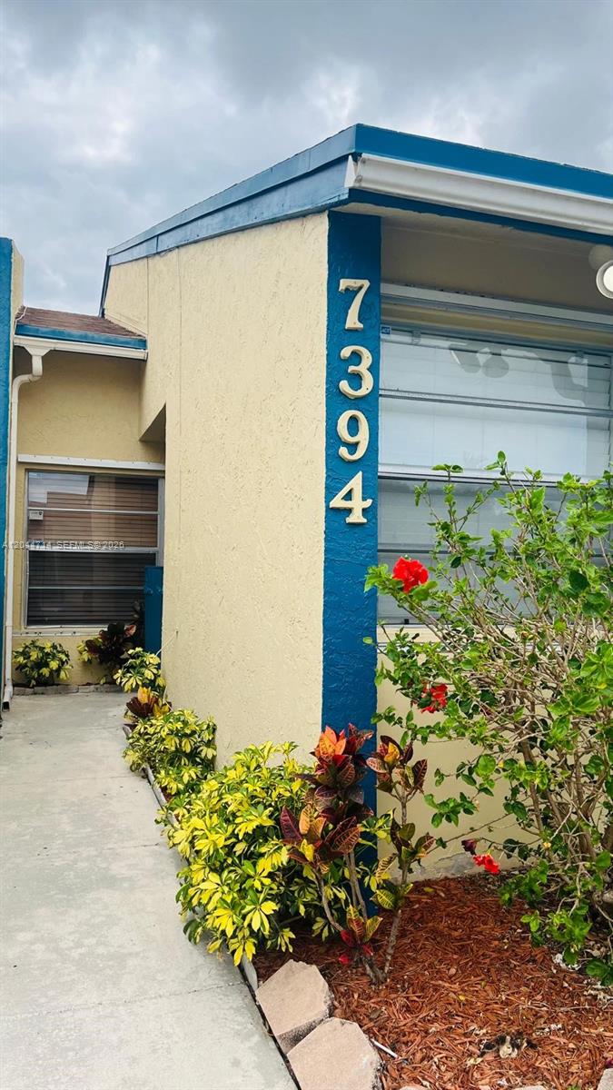 The exterior of a house features a yellow stucco wall, blue trim, and landscaping — 7394 NW 34th St, Lauderhill FL 33319, LAUDERHILL, FL