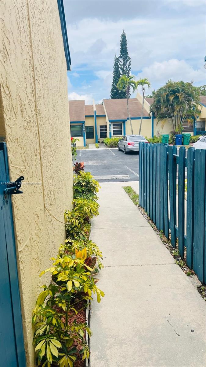 A concrete walkway leads past a yellow building and a blue fence toward a parking lot — 7394 NW 34th St, Lauderhill FL 33319, LAUDERHILL, FL