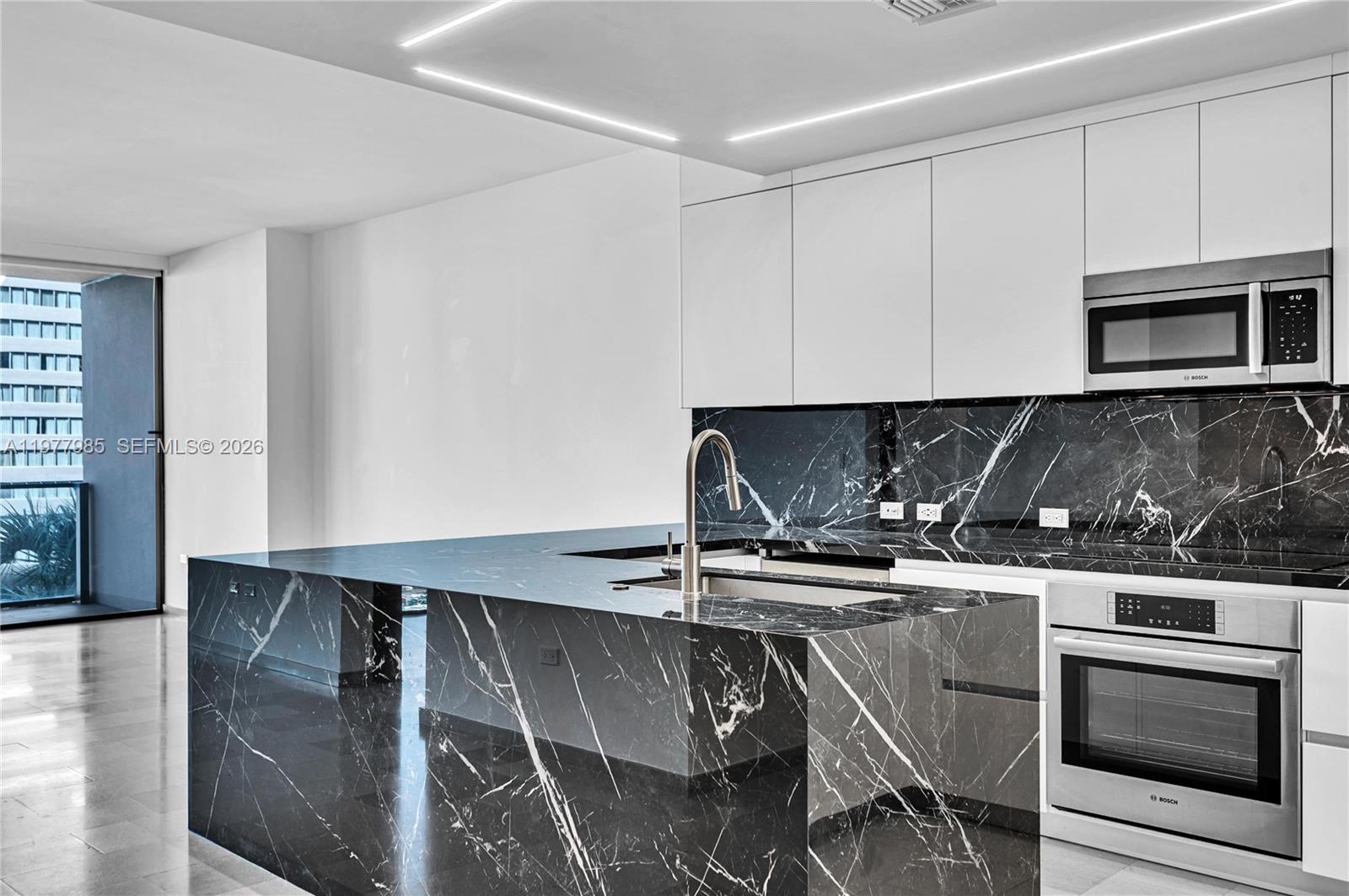 A modern kitchen features black marble countertops and backsplash with white cabinetry and stainless appliances — 88 SW 7th St # 806, Miami FL 33130, MIAMI, FL